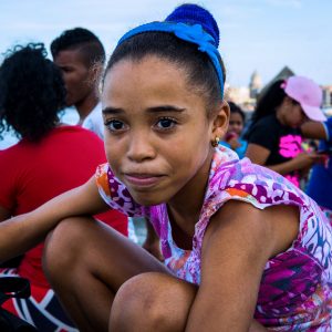 Young girl sitting along the boardwalk by the sea in Havana.